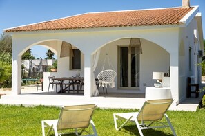 A white building with a tiled roof, a covered patio with outdoor furniture, and a hanging chair. - Villa Bianca (Avola)