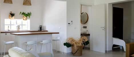 A modern kitchen with white bar stools, a central island, and hanging plants.