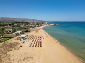 An aerial view of a beach with rows of sun loungers and umbrellas, a clear blue sky, and a calm sea. - Villa Bianca (Avola)