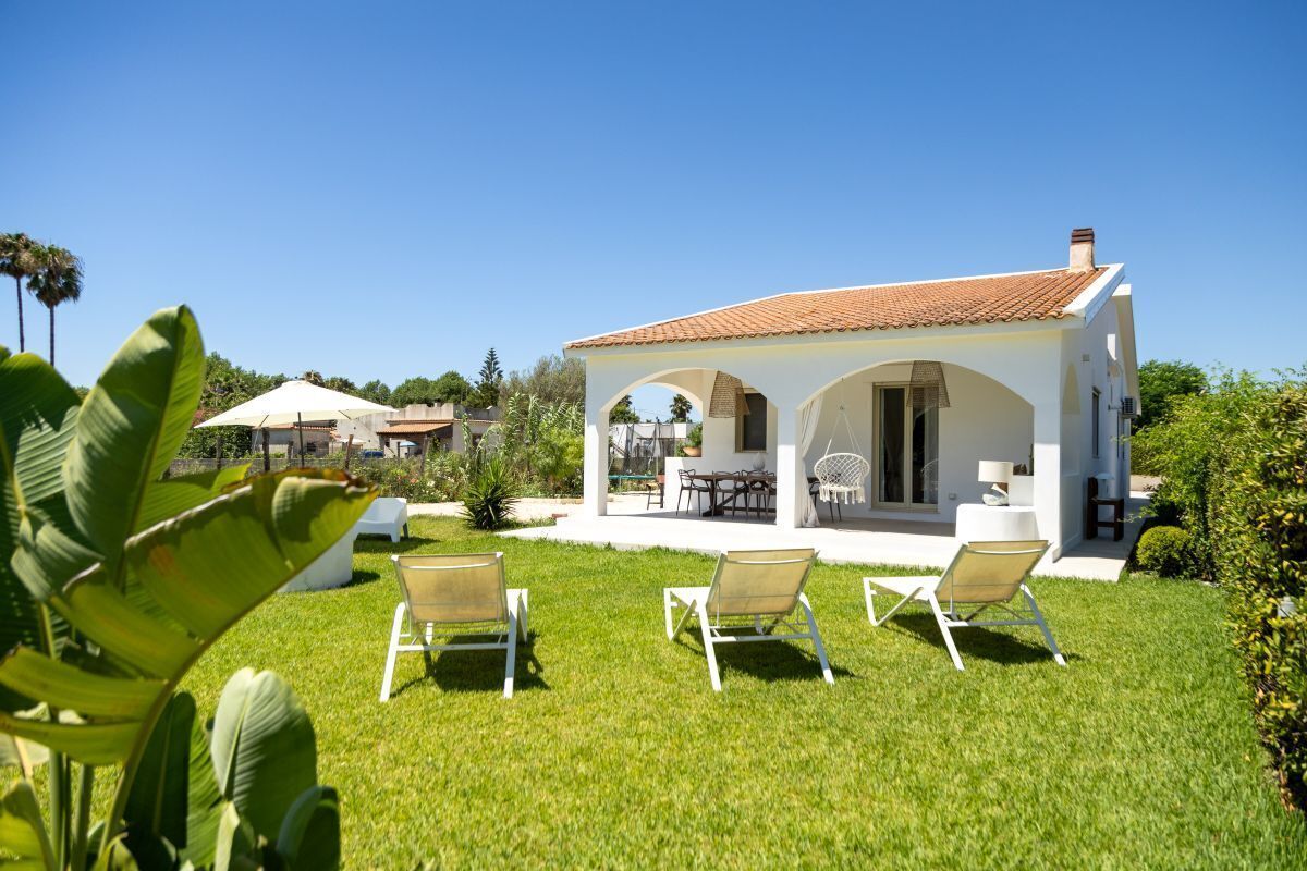 Une maison moderne avec un toit en tuiles, une terrasse dotée de mobilier d’extérieur et une pelouse bien entretenue.