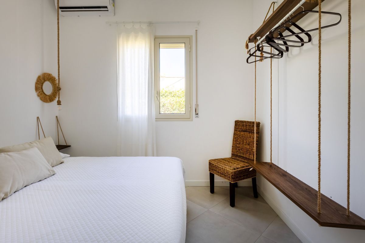 A bedroom with a bed, a chair, a window, and a wall-mounted rack.