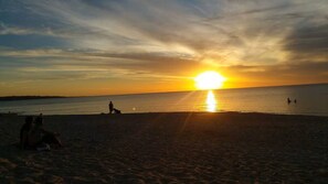 A beach scene with the sun setting over the horizon, people sitting and walking along the shore. - Modern 3 Bed, 2.5 Bathroom House by the Beach (Seaford)