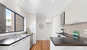 A modern kitchen with white cabinetry, a granite countertop, and a built-in stove. - Modern 3 Bed, 2.5 Bathroom House by the Beach (Seaford)