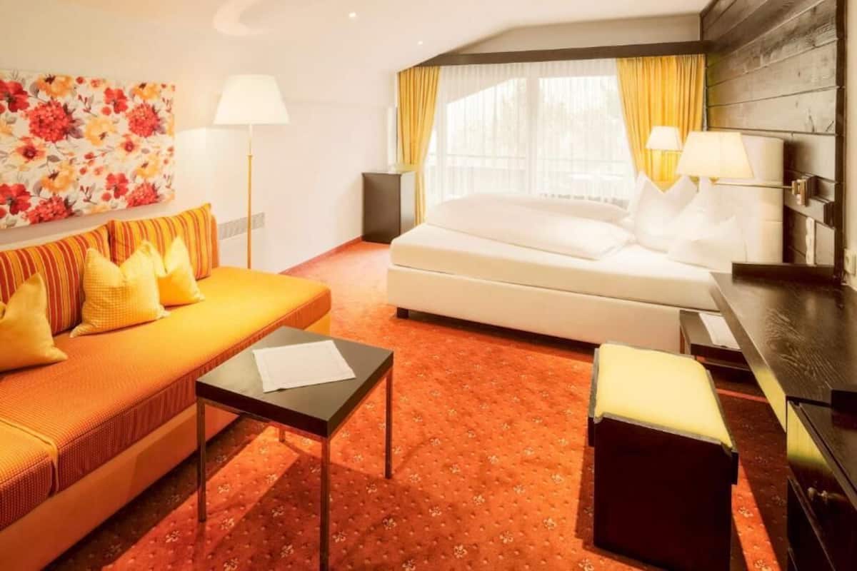 A hotel room with a sofa, a bed, a small table, and a lamp.