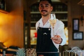 A person holding a champagne flute, a pineapple, and a glass of what appears to be a cocktail. - Hotel Pfeifer (Gaschurn)
