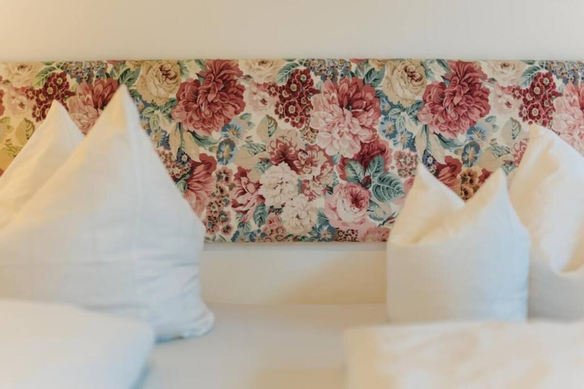 A bed with white pillows and a floral-patterned headboard.