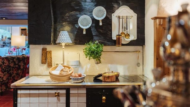 Une cuisine avec un crédence noir, des ustensiles de cuisine suspendus, une plante et un dosseret carrelé.