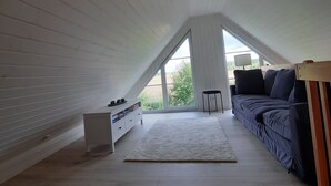 A room with a sloped ceiling, a sofa, a small table, and a cabinet.