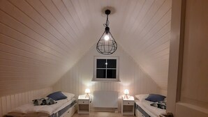 A room with two beds, a window, a radiator, and a hanging light fixture.