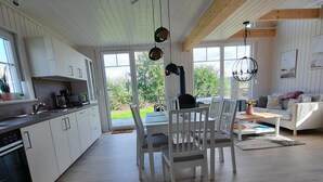 A spacious kitchen with white cabinets, a dining area with white chairs, and a large window offering a view of the outdoors.