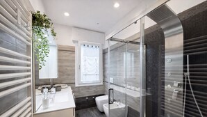 Un baño moderno con ducha de vidrio, lavamanos blanco y un inodoro.