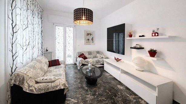 Una sala de estar moderna con un sofá, una mesa de centro, una lámpara colgante y una consola blanca con objetos decorativos.
