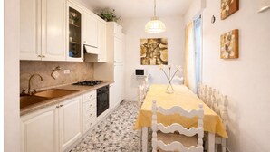 Una cocina con armarios blancos, encimera de granito, una mesa de comedor cubierta con mantel amarillo y una lámpara colgante.