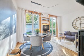 Ein modernes Wohnzimmer mit Essbereich, großen Fenstern, einem Kamin und einer Wanduhr.