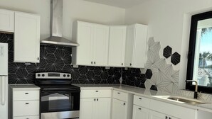A modern kitchen with white cabinetry, a stainless steel oven, and a black backsplash. - Lighthouse (Flagler Beach)
