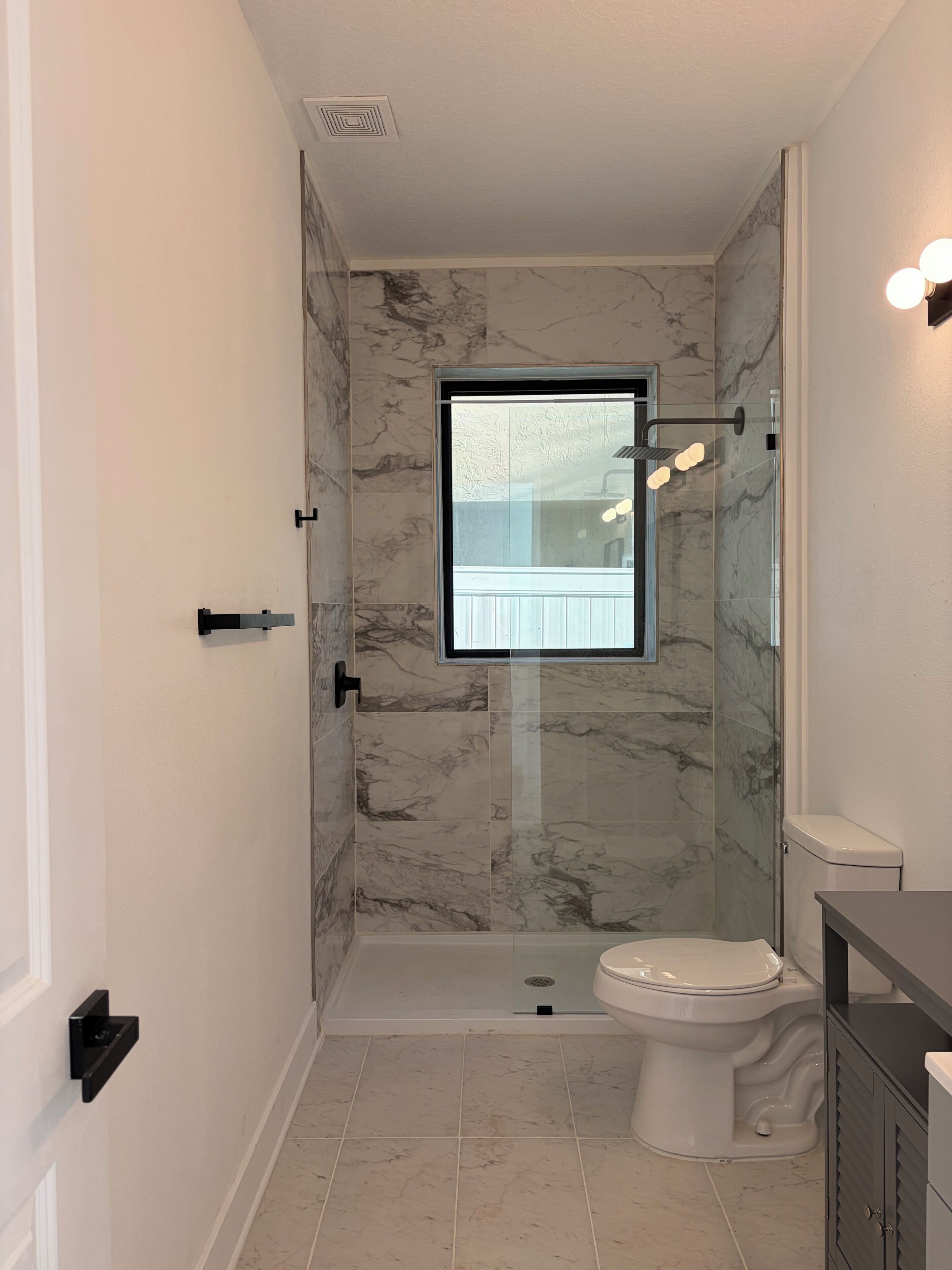 A bathroom with a glass-enclosed shower, a toilet, and a vanity with a mirror.