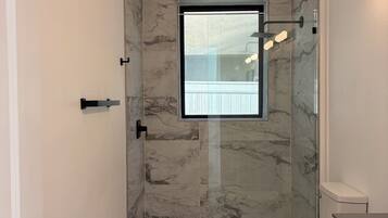 A bathroom with a glass-enclosed shower, a toilet, and a vanity with a mirror.