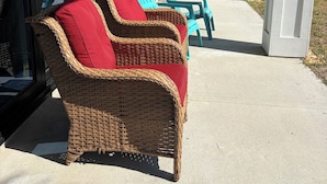A covered outdoor seating area with wicker furniture and cushions. - Lighthouse (Flagler Beach)