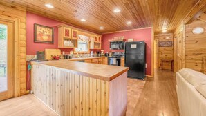 A cabin interior with a wooden ceiling, a kitchen area including a refrigerator, a microwave, and a sink, and a wooden bar counter. - At Birch Hollow, we aim to provide a harmonious blend of tranquility, adventure, and comfort (Stanton)