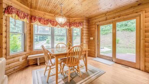 A wooden cabin interior with a dining table, chairs, a chandelier, and large windows offering a view of the outdoors. - At Birch Hollow, we aim to provide a harmonious blend of tranquility, adventure, and comfort (Stanton)
