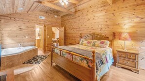 A wooden cabin bedroom with a bed, a nightstand, a lamp, and a bathroom with a bathtub. - At Birch Hollow, we aim to provide a harmonious blend of tranquility, adventure, and comfort (Stanton)