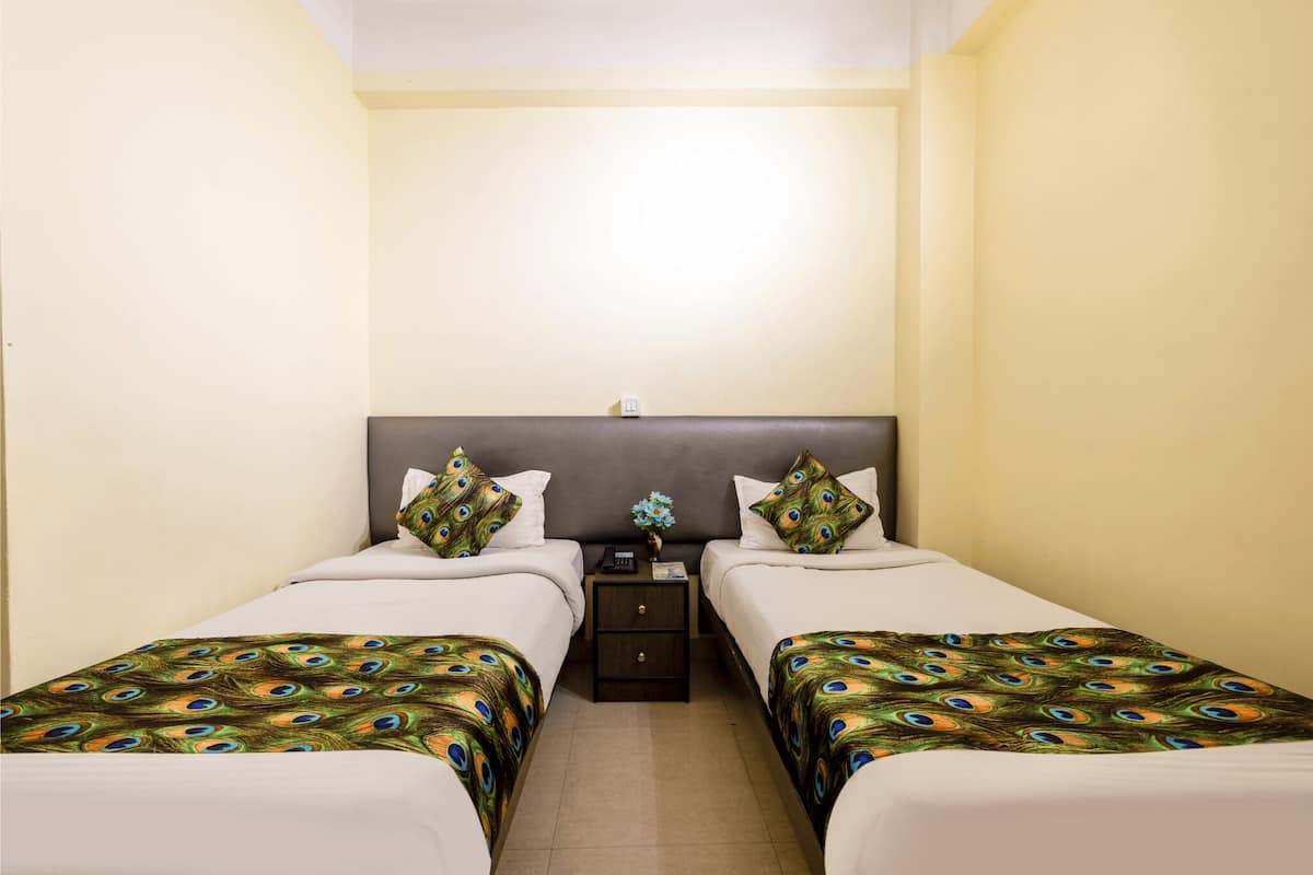 A hotel room with two single beds, each with a peacock feather bedspread, a nightstand between them, and a small table with a vase of flowers.