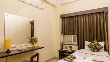 A hotel room with a bed, a desk with a chair, a mirror, a ceiling fan, and a window with curtains.