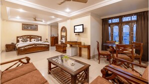 A well-lit room with a bed, a desk, a television, and a dining area with chairs and a table. - Mayur Hotel (Guwahati)