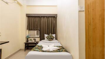 A hotel room with a bed, a bedside table, an air conditioning unit, and a wooden door.