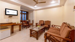 A living room with a television, wooden furniture, a ceiling fan, and a dining area with chairs and a table. - Mayur Hotel (Guwahati)