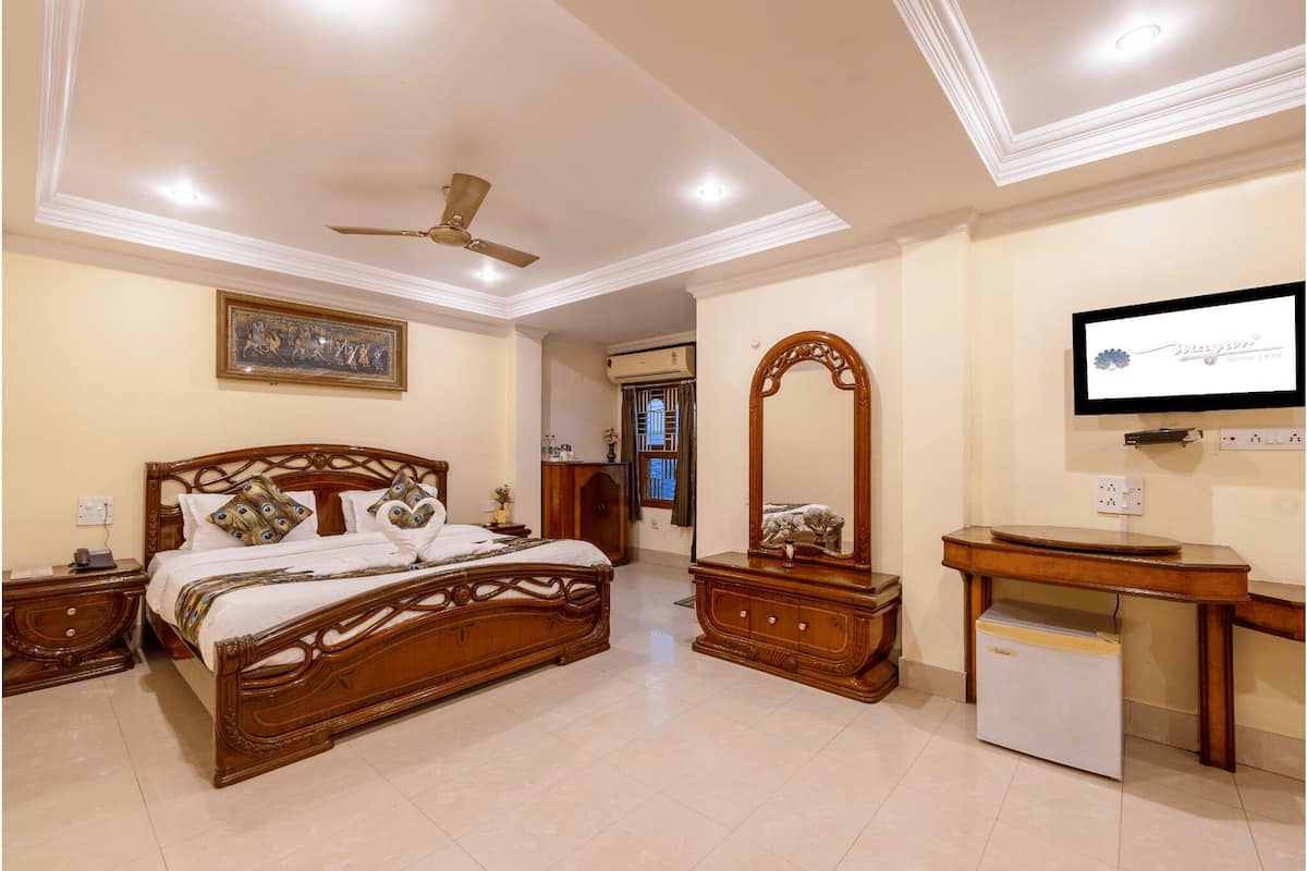 A bedroom with a wooden bed, a ceiling fan, a TV, and a small refrigerator.