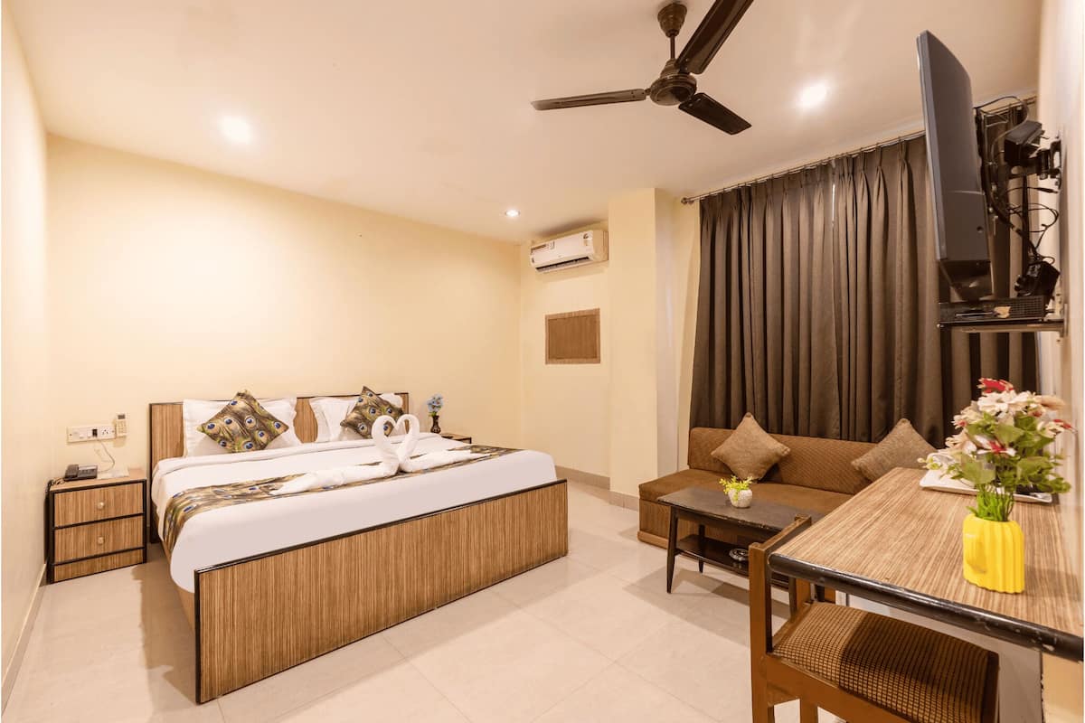A hotel room with a bed, a sofa, a TV, and a table with a vase of flowers.
