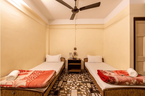 A small, clean room with two single beds, a ceiling fan, and a tiled floor. - Mayur Hotel (Guwahati)
