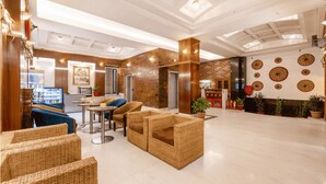 A spacious lobby with wicker furniture, a brick wall, and decorative plates on the wall. - Mayur Hotel (Guwahati)