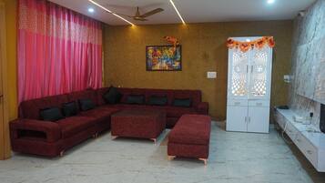 A living room with a sectional sofa, a coffee table, and an ottoman. There is a white cabinet with decorative elements on the wall, and a ceiling fan.