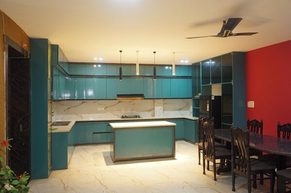 A modern kitchen with teal cabinets, a marble countertop, and a dining area with a black table and wooden chairs.