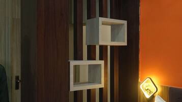 Un dormitorio con cama, una mesita de noche con lámpara y un armario de madera con estantes.