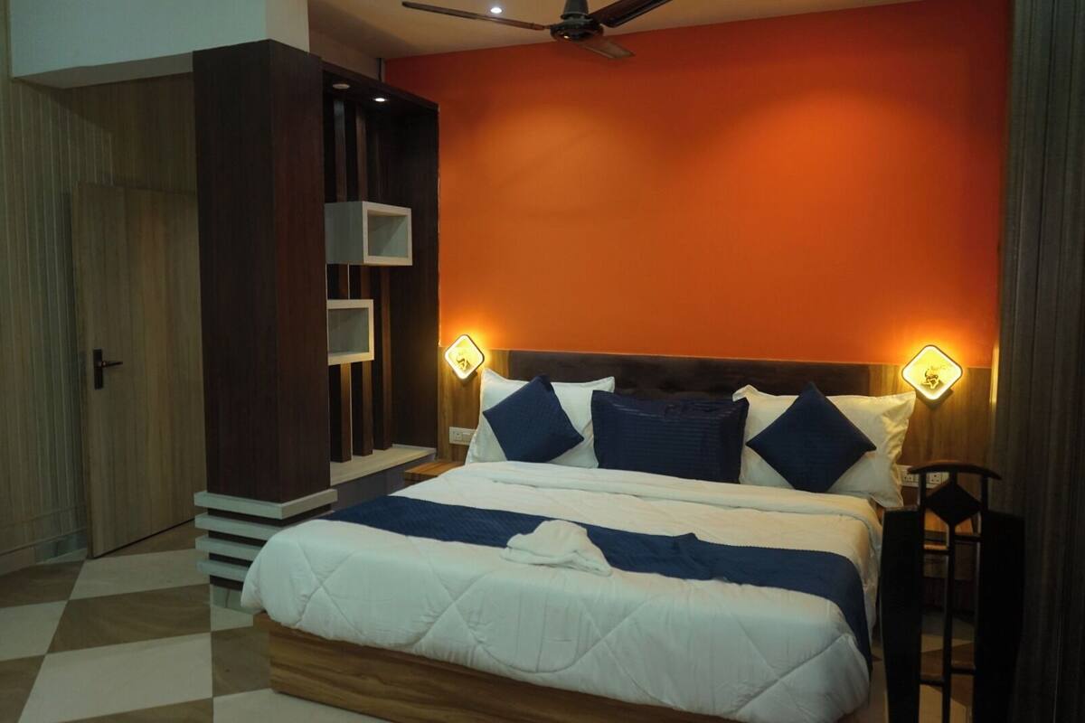 A hotel room with a large bed, two bedside tables, a ceiling fan, and an orange accent wall.