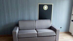 Ett rum med en grå soffa, trägolv och en grå vägg med vertikala linjer.