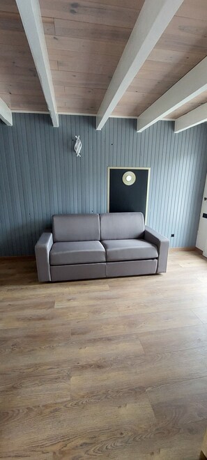 Une pièce avec un canapé gris, un plancher en bois et un mur gris orné de lignes verticales.