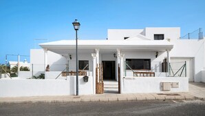 Un edificio blanco con un porche cubierto, una farola y un acceso con portones.