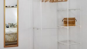 Un armario blanco con estantes, barra para colgar ropa y espejo.