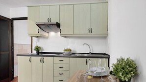 Una cocina con armarios verde claro, encimera negra, campana extractora de acero inoxidable, un lavamanos y una zona de comedor con una mesa preparada para dos.