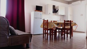 A compact living space with a sofa, a dining table with chairs, a kitchen area with cabinets and a refrigerator, and a television on top of the fridge. - Residence Marino (Balestrate)