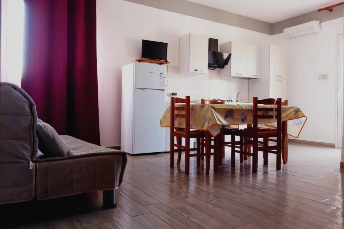 A compact living space with a sofa, a dining table with chairs, a kitchen area with cabinets and a refrigerator, and a television on top of the fridge.