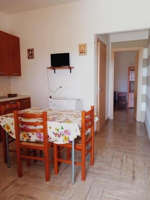 A dining area with a table covered in a floral tablecloth, surrounded by wooden chairs. A television is mounted on the wall above the table. - Residence Marino (Balestrate)