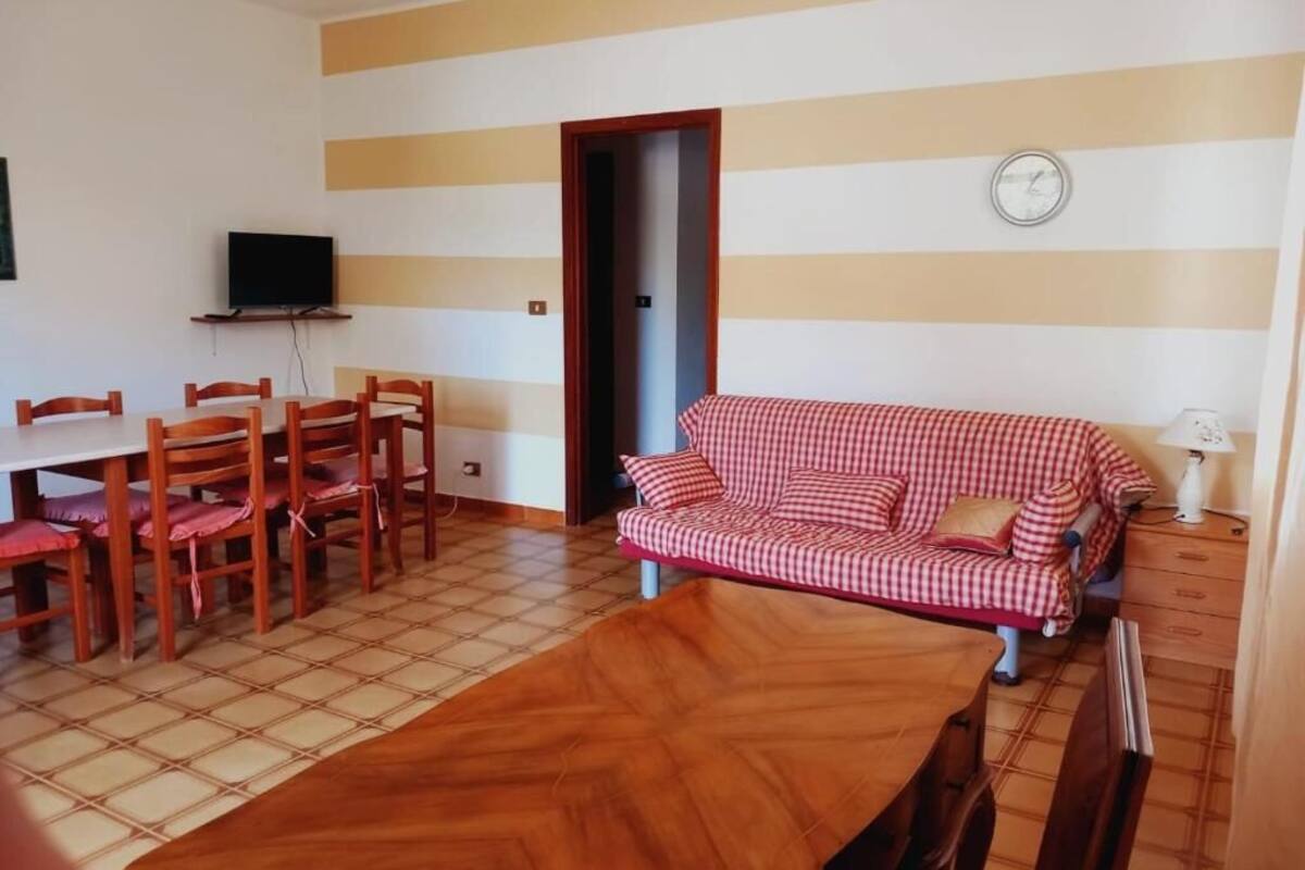 A living room with a wooden dining table, chairs, a red checkered sofa, and a television on a stand.