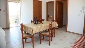 A dining area with a checkered tablecloth, wooden chairs, and a bowl of fruit and bottles. - Residence Marino (Balestrate)