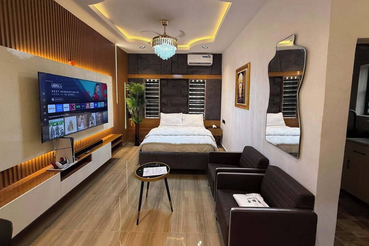 A modern hotel room with a large flat-screen TV, a bed, a sofa, a small table, and a mirror.