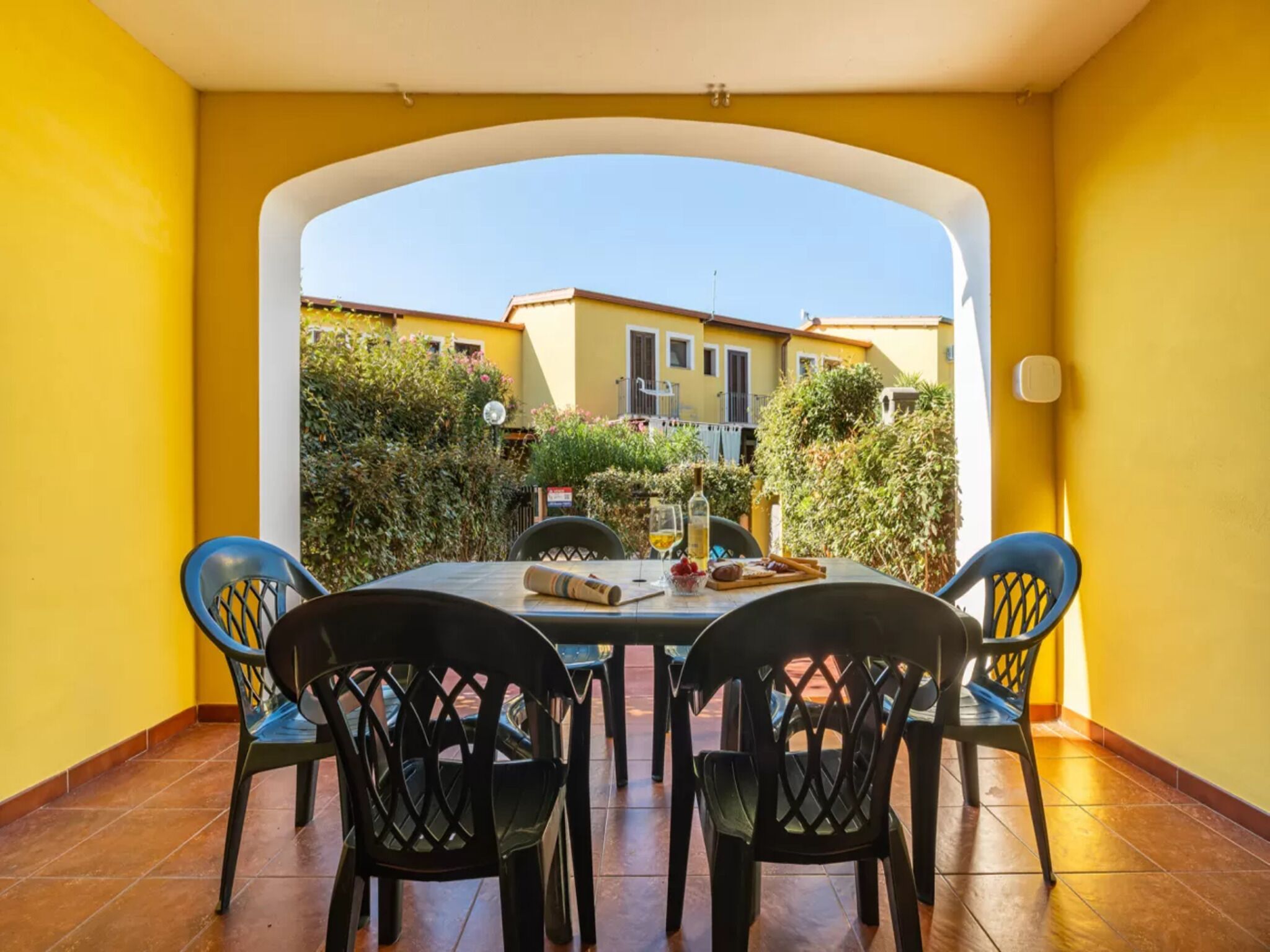 Varanda com mesa e cadeiras, vista para prédios e piso de azulejos.